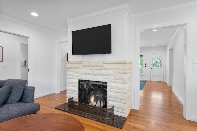 living room with light wood-type flooring, ornamental molding, baseboards, and a stone fireplace