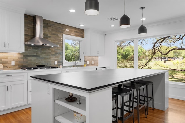 kitchen featuring a center island, tasteful backsplash, open shelves, stainless steel gas stovetop, and wall chimney exhaust hood