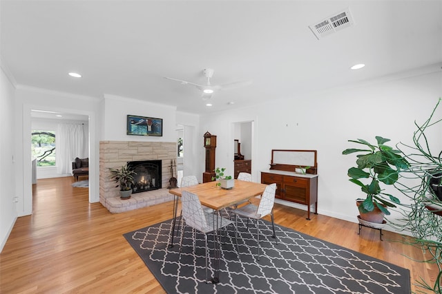 dining room featuring visible vents, crown molding, a fireplace, baseboards, and light wood-style flooring