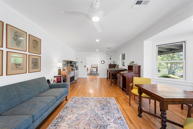 living room with light wood-style floors, ornamental molding, a ceiling fan, and visible vents