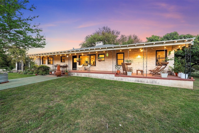 back of property at dusk with a lawn, a chimney, covered porch, and stone siding