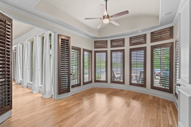 empty room with a raised ceiling, a ceiling fan, wood finished floors, and a wealth of natural light