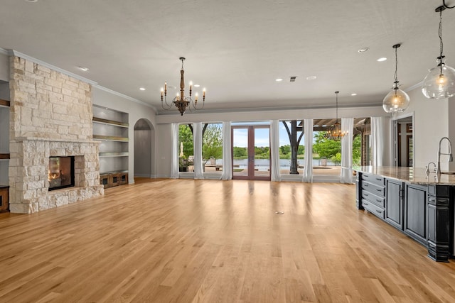 unfurnished living room featuring a fireplace, a chandelier, built in shelves, light wood-style flooring, and ornamental molding