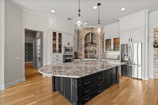 kitchen with dark cabinets, appliances with stainless steel finishes, wall chimney range hood, and white cabinetry