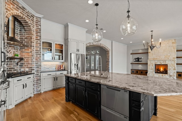kitchen with a sink, white cabinets, ornamental molding, stainless steel appliances, and an island with sink
