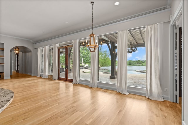 unfurnished dining area with a water view, a notable chandelier, ornamental molding, and plenty of natural light