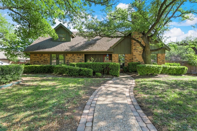 view of front of property with brick siding, a shingled roof, a front lawn, and fence