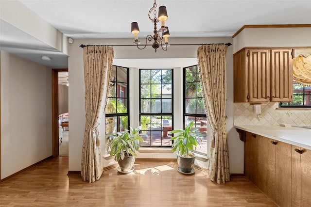 unfurnished dining area with baseboards, an inviting chandelier, and light wood-style floors