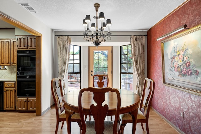 dining space with a textured ceiling, a chandelier, visible vents, and light wood-type flooring