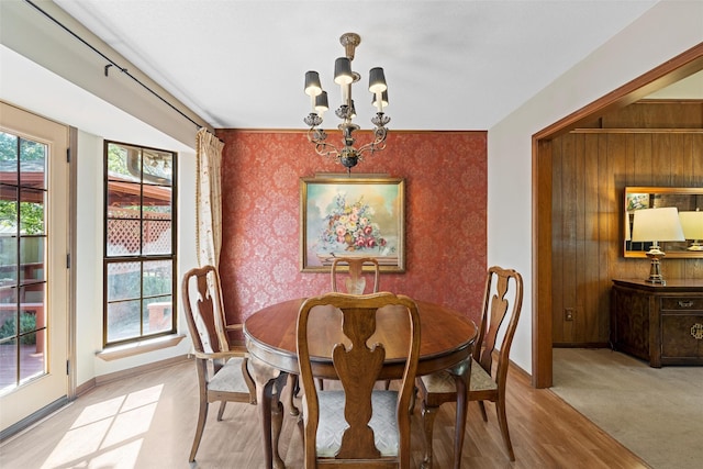 dining room with an accent wall, wallpapered walls, light wood-type flooring, baseboards, and a notable chandelier