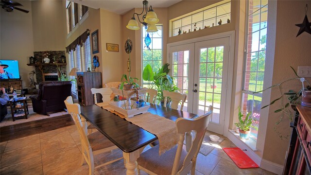 tiled dining area with a fireplace, a healthy amount of sunlight, a ceiling fan, and french doors