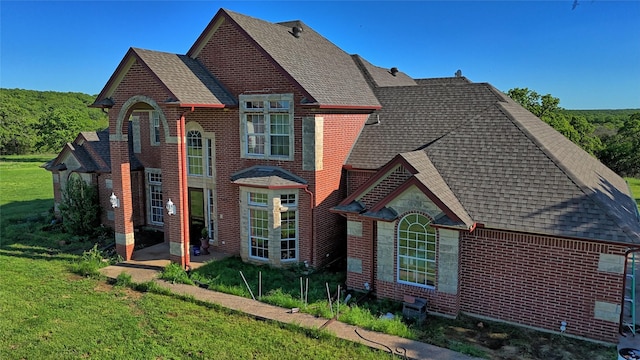exterior space with a patio area, a shingled roof, brick siding, and a front yard