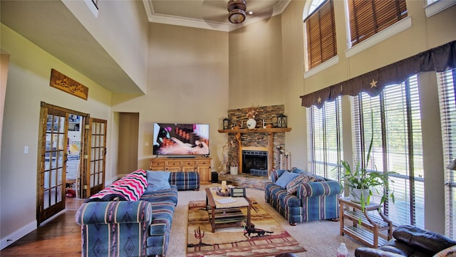 living area featuring a high ceiling, a stone fireplace, french doors, crown molding, and ceiling fan