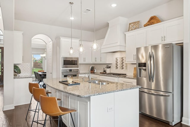 13002 Clarendon Dr, Frisco, TX 75035 - kitchen with a sink, a kitchen island with sink, white cabinetry, appliances with stainless steel finishes, and custom exhaust hood