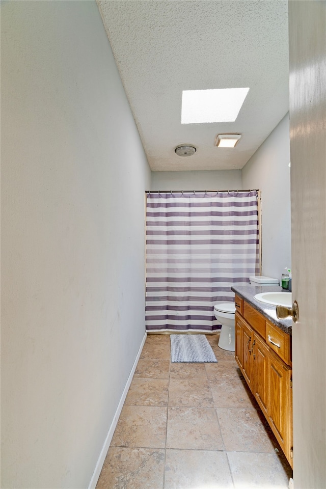 full bath with toilet, a textured ceiling, a skylight, vanity, and baseboards