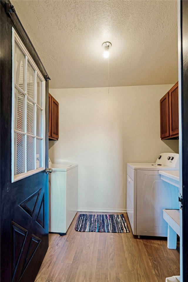 laundry room featuring wood finished floors, washer and clothes dryer, a textured ceiling, cabinet space, and baseboards