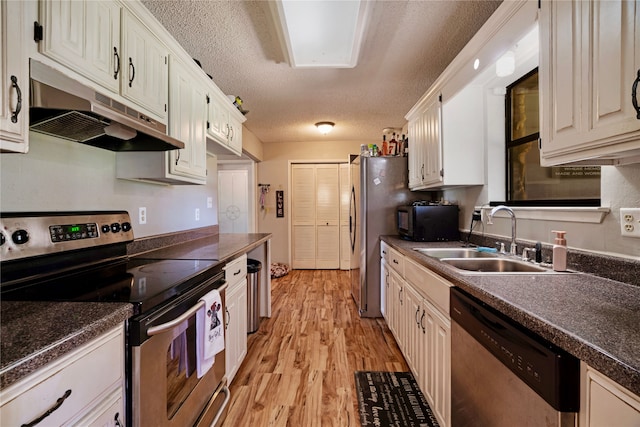 kitchen with a textured ceiling, a sink, light wood-style floors, under cabinet range hood, and appliances with stainless steel finishes