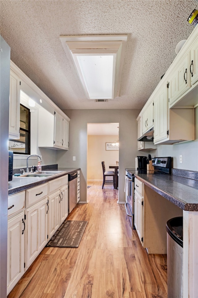kitchen with stainless steel appliances, light wood-style flooring, a sink, dark countertops, and visible vents