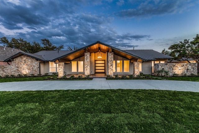 view of front facade featuring a front yard, a standing seam roof, metal roof, and stone siding