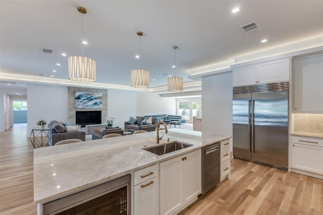 kitchen with visible vents, a sink, open floor plan, built in appliances, and light wood-style flooring
