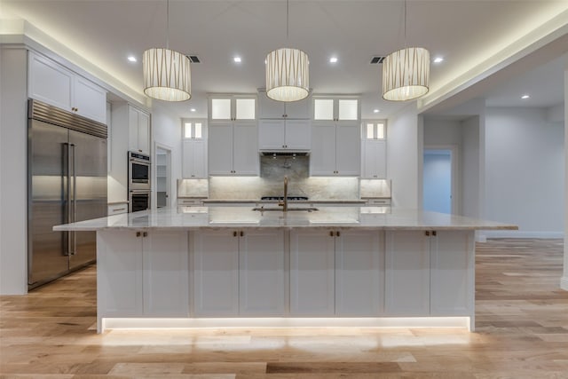 kitchen featuring light stone countertops, white cabinets, a large island with sink, backsplash, and stainless steel appliances