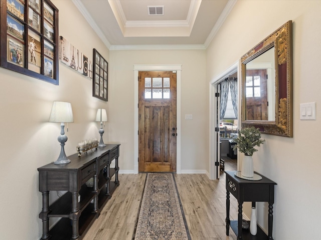 entryway with a tray ceiling, visible vents, ornamental molding, light wood-type flooring, and baseboards