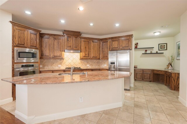 8316 Lindsay Gdns, The Colony, TX 75056 - kitchen with stainless steel appliances, under cabinet range hood, brown cabinets, tasteful backsplash, and light stone counters