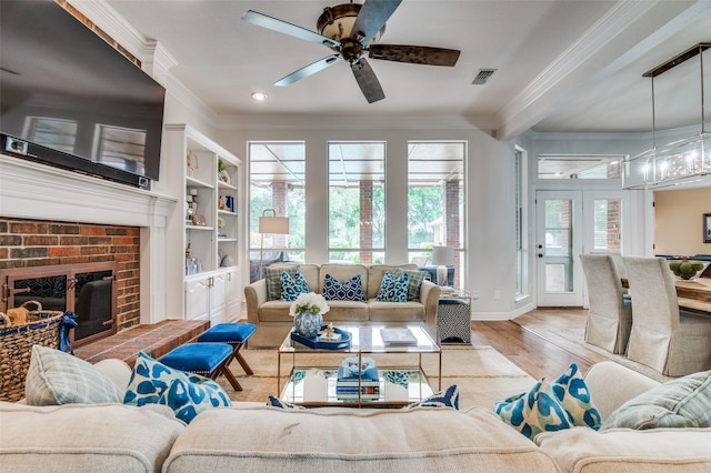living room with wood finished floors, visible vents, a ceiling fan, ornamental molding, and baseboards