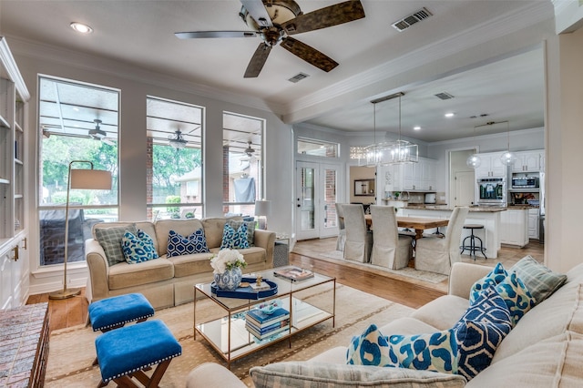 living area featuring light wood finished floors, a ceiling fan, visible vents, and ornamental molding