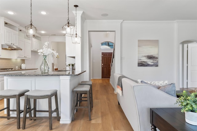 kitchen with a breakfast bar, dark stone counters, white cabinetry, backsplash, and under cabinet range hood