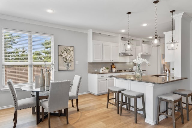 kitchen featuring a kitchen bar, tasteful backsplash, stainless steel gas cooktop, light wood-type flooring, and a sink