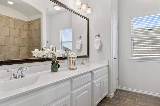 bathroom with a sink, a tile shower, double vanity, and wood finish floors