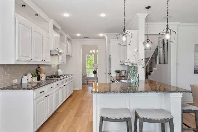 kitchen featuring a kitchen breakfast bar, backsplash, a peninsula, light wood finished floors, and white cabinetry