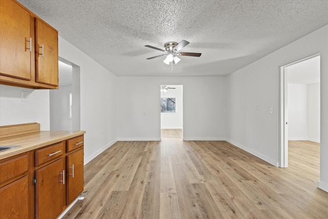 interior space with light wood-style floors, a textured ceiling, a ceiling fan, and baseboards