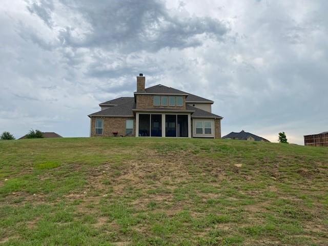 rear view of house featuring a yard, a sunroom, and a chimney