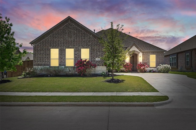 french provincial home featuring fence, brick siding, a yard, and concrete driveway
