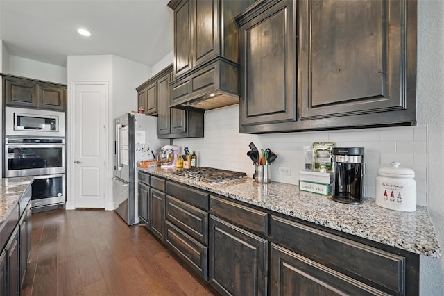 kitchen with backsplash, dark wood-type flooring, light stone countertops, dark brown cabinetry, and appliances with stainless steel finishes