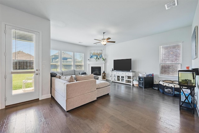 living area with dark wood-style floors, a glass covered fireplace, baseboards, visible vents, and ceiling fan