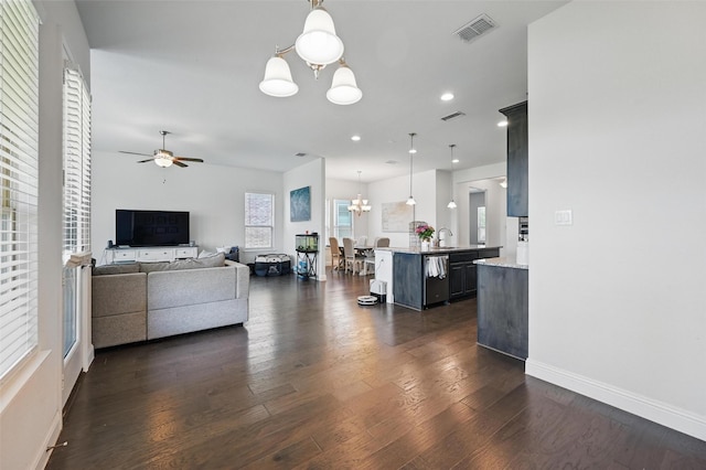 living area featuring baseboards, a healthy amount of sunlight, visible vents, and ceiling fan with notable chandelier