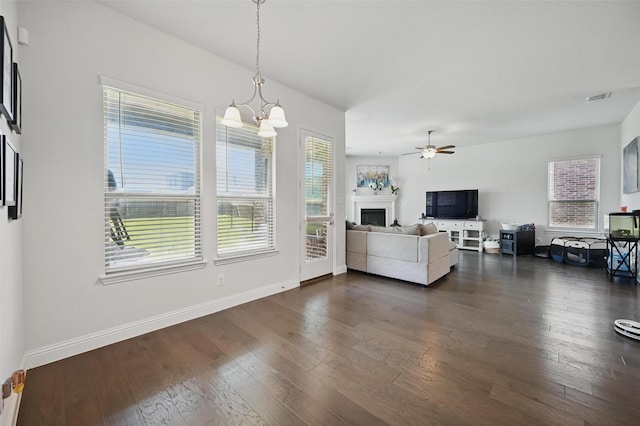 living area featuring a fireplace, plenty of natural light, visible vents, and ceiling fan with notable chandelier