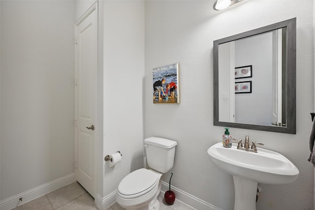 half bathroom featuring toilet, tile patterned flooring, a sink, and baseboards