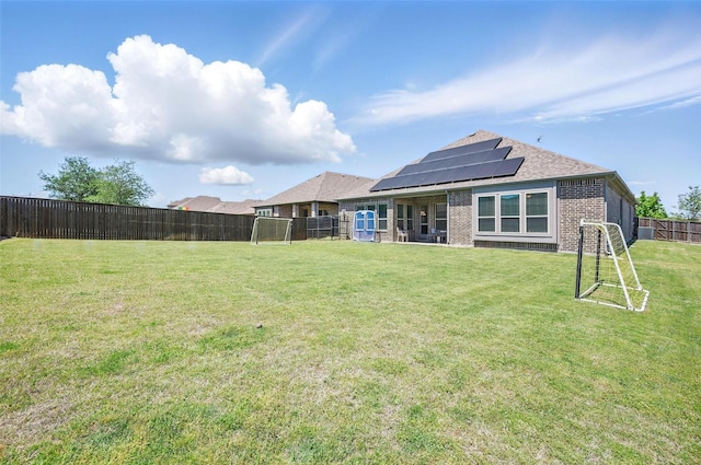 rear view of house with roof with shingles, a fenced backyard, brick siding, a yard, and roof mounted solar panels