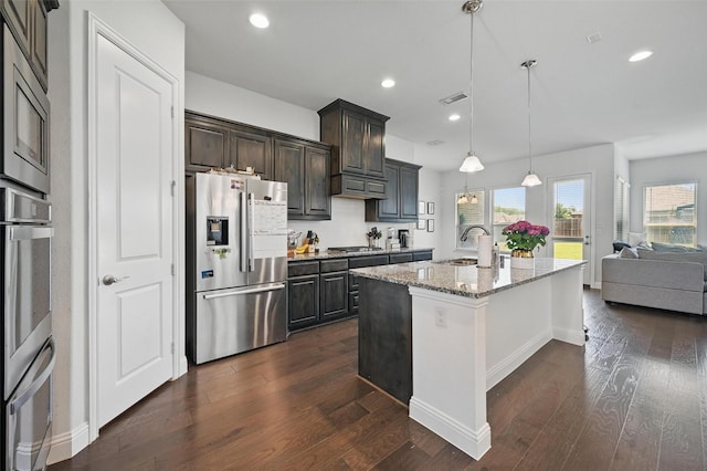 kitchen with a sink, recessed lighting, light stone countertops, dark wood-type flooring, and appliances with stainless steel finishes