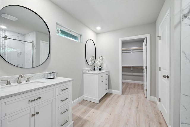 bathroom with wood finished floors, a sink, a marble finish shower, a spacious closet, and two vanities