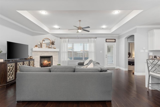living room featuring ceiling fan, a raised ceiling, and dark wood finished floors