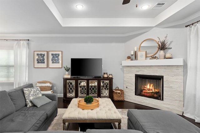 living area featuring visible vents, wood finished floors, ceiling fan, a stone fireplace, and ornamental molding