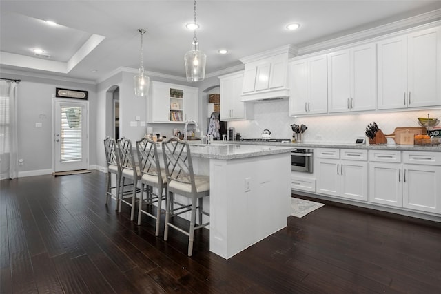 kitchen featuring arched walkways, dark wood-style flooring, a breakfast bar area, and decorative backsplash