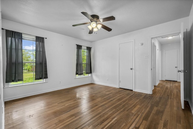 unfurnished bedroom featuring baseboards, a ceiling fan, dark wood-style floors, and multiple windows