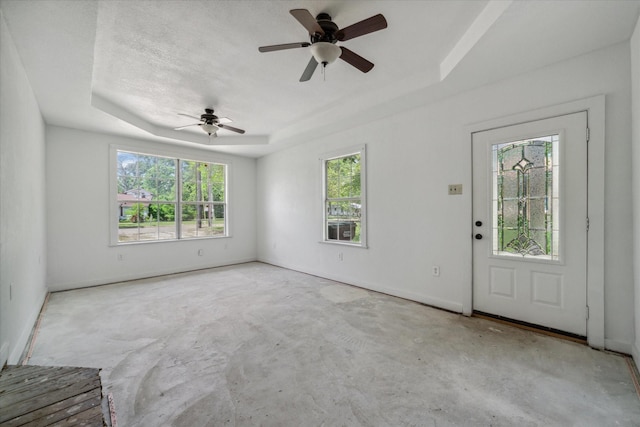 foyer with a ceiling fan, a tray ceiling, and concrete flooring