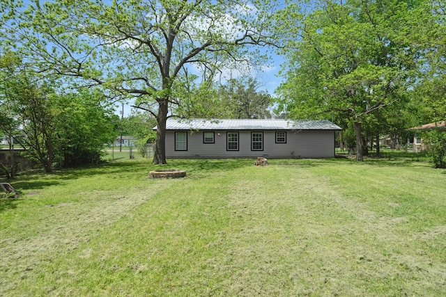 back of property with fence, a lawn, an outdoor fire pit, and metal roof